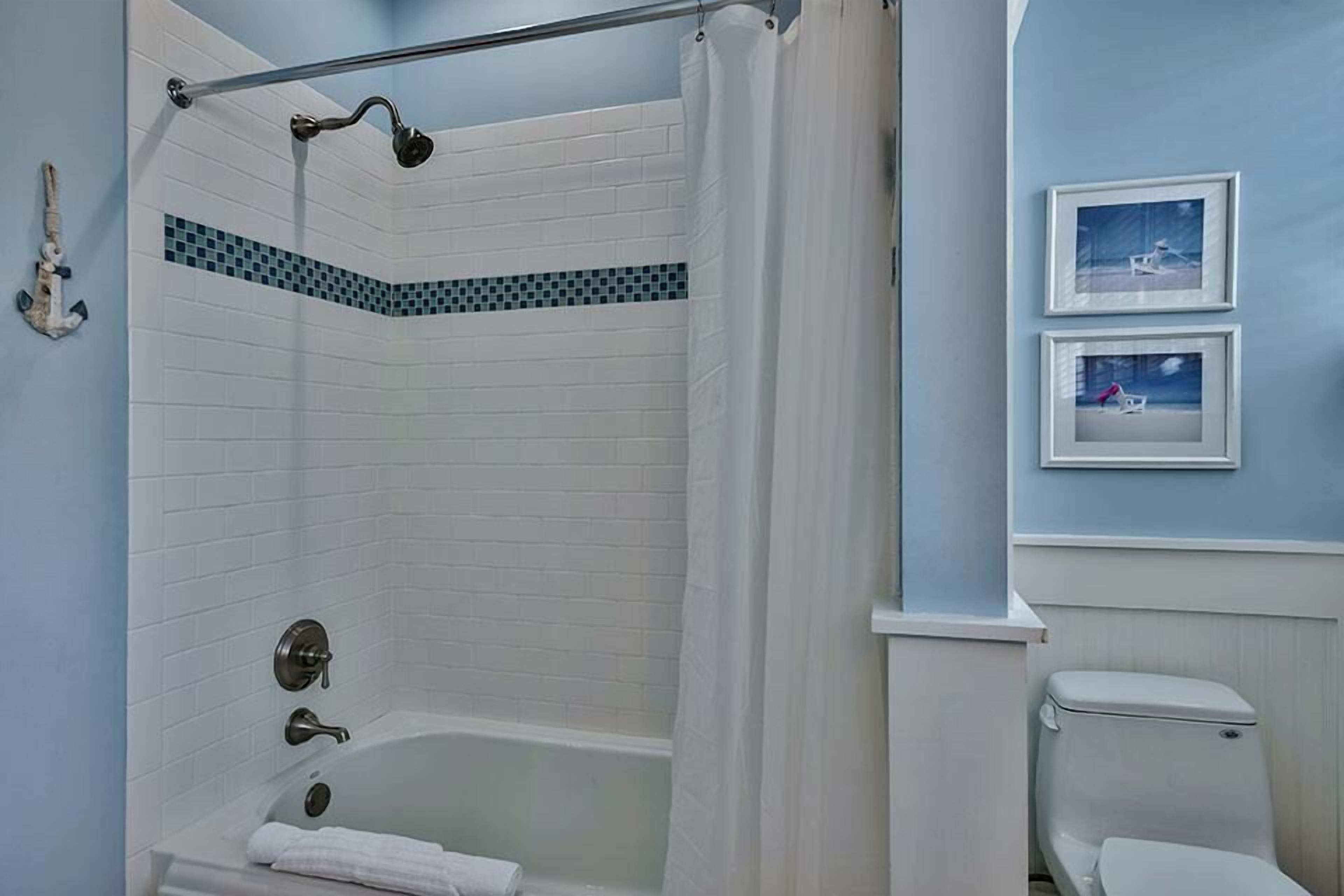 Een badkamer met een bad, douche en toilet. Twee afbeeldingen hangen in lijsten aan de muur.