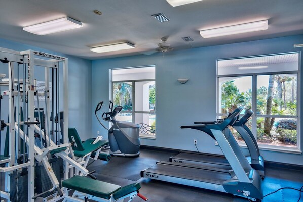 A gym with treadmills, exercise machines, and large windows offering views of greenery.