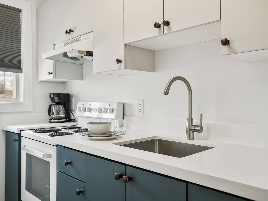 Una cocina moderna con armarios blancos, un lavamanos de acero inoxidable y un horno empotrado.