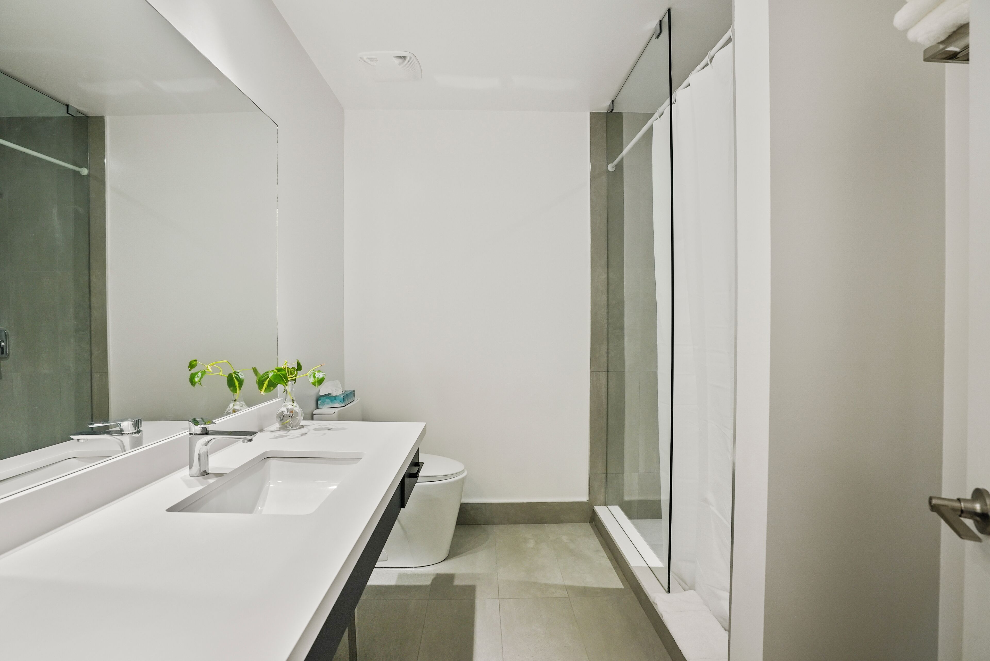 A modern bathroom with a white vanity, two sinks, a toilet, and a glass shower enclosure.
