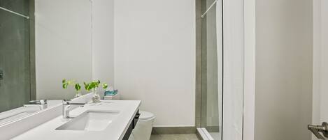 A modern bathroom with a white vanity, two sinks, a toilet, and a glass shower enclosure.