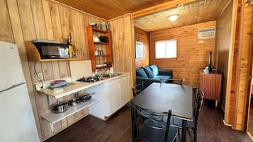 Una cocina compacta con paredes de madera, un microondas, un fregadero y una zona de comedor con mesa y sillas.