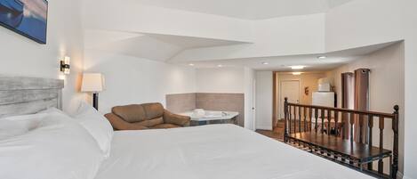 Un dormitorio amplio con una cama grande, una zona de estar con un sofá, una mesita y un jacuzzi.
