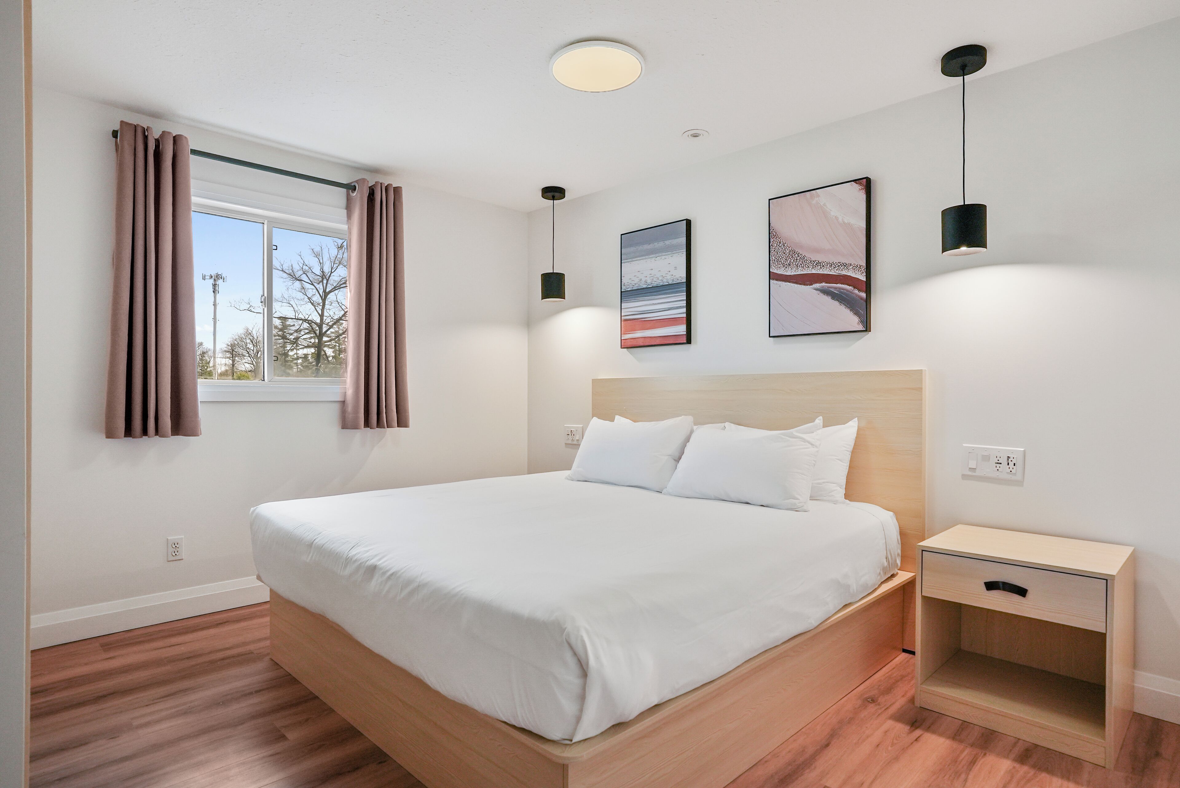 A modern bedroom with a wooden bed, white bedding, a nightstand, and a window with curtains.