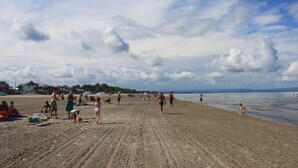 A sandy beach with people walking and playing, umbrellas, and a clear sky. - Saga Resort (Wasaga Beach)