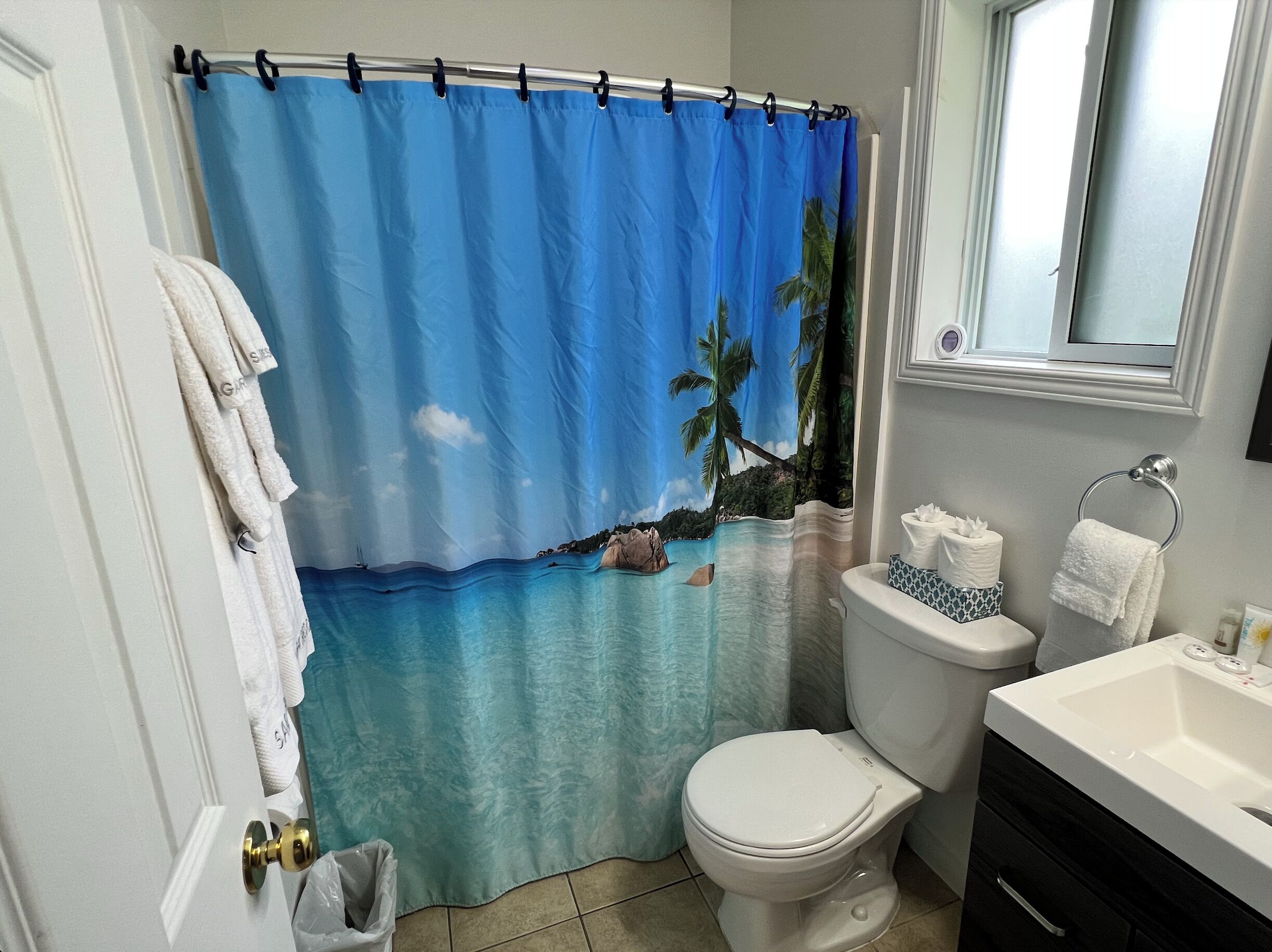 Ein Badezimmer mit Duschvorhang mit Strandmotiv, Toilette, Waschbecken und Spiegel.