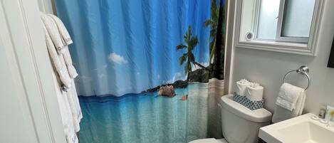 Ein Badezimmer mit Duschvorhang mit Strandmotiv, Toilette, Waschbecken und Spiegel.