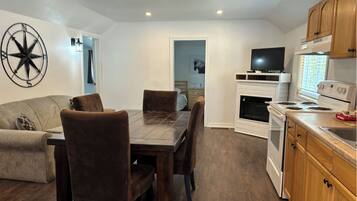 Een moderne keuken met een eethoek, met een grote houten tafel, donkerbruine stoelen, een televisie en een fornuis.