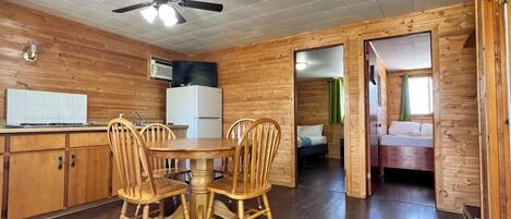 A wooden cabin with a kitchen area, dining table, and two bedrooms.