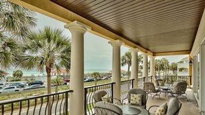 A covered outdoor seating area with tables and chairs, palm trees, and a view of the ocean and parked cars. - Sea Span 6 Bedroom Holiday Home by Five Star Properties (Destin)