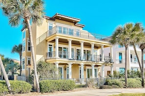 A multi-story building with a balcony on the second floor, surrounded by palm trees and a well-maintained lawn.
