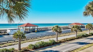 A coastal road with a beachside walkway, palm trees, and two red-roofed structures. - Sea Span 6 Bedroom Holiday Home by Five Star Properties (Destin)