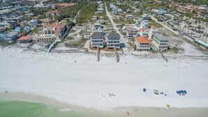 Vista aérea de una zona residencial costera con propiedades frente al mar, incluyendo casas con balcones y una playa en primer plano.