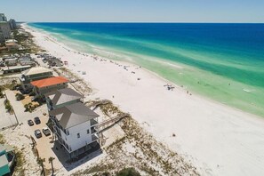 A beachfront property with a large white building, a sandy beach, and a clear blue ocean.