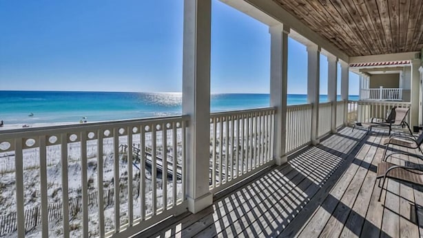 A covered outdoor area with a wooden ceiling and white railings, overlooking a beach with sand and sparse vegetation. - Seaclusion 9 Bedroom Holiday Home by Five Star Properties (Miramar Beach)