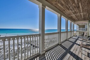 A covered outdoor area with a wooden ceiling and white railings, overlooking a beach with sand and sparse vegetation. - Seaclusion 9 Bedroom Holiday Home by Five Star Properties (Miramar Beach)