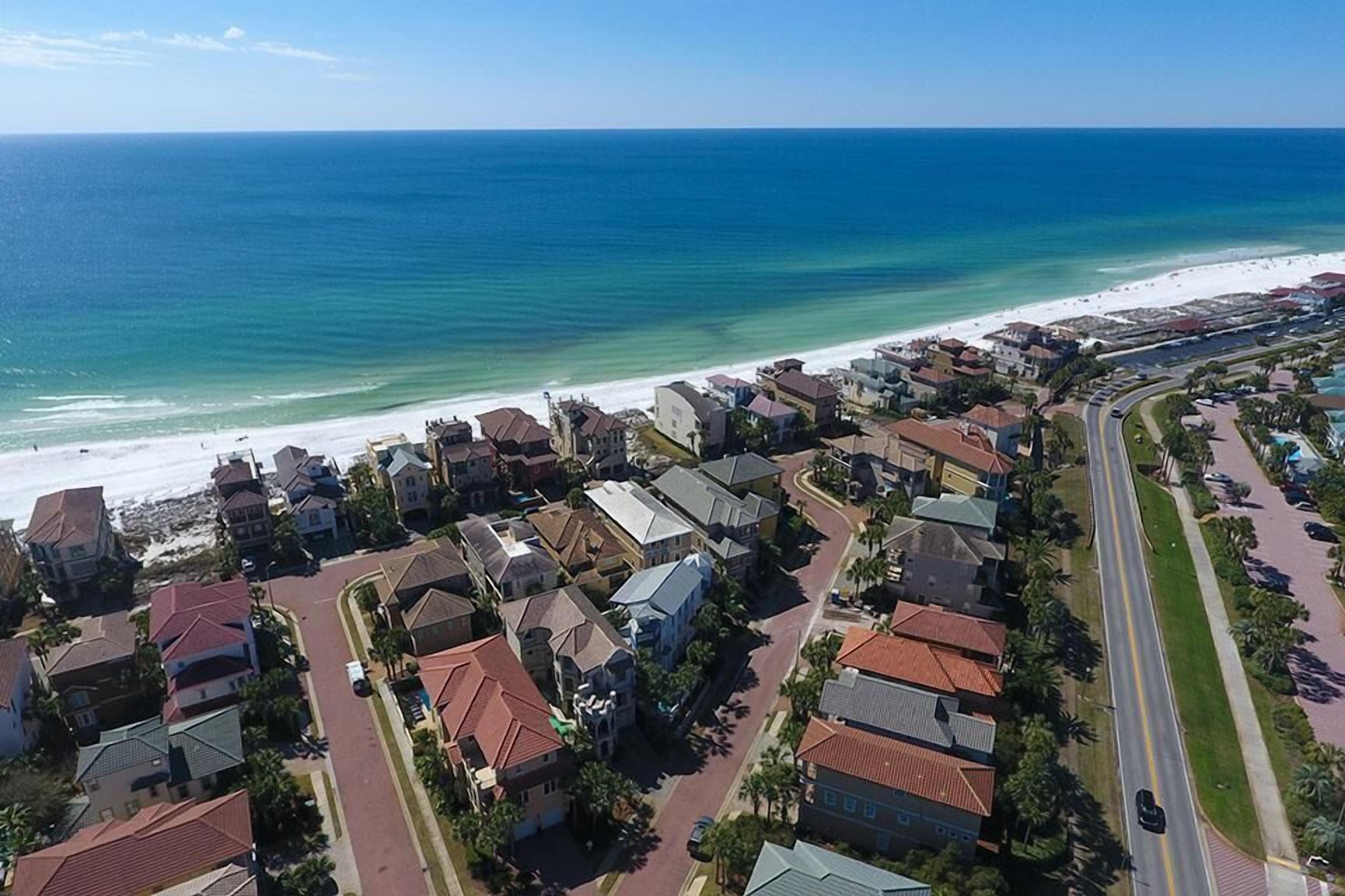 Vue aérienne d’une zone résidentielle côtière, avec des maisons, une plage et une route.