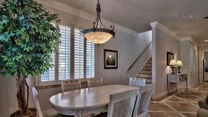 A dining area with a round table, chairs, a hanging light fixture, a potted plant, and a staircase in the background. - Serenity 4 Bedroom Holiday Home by Five Star Properties (Destin)