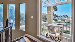 Un balcon avec vue sur la plage, une table en bois et deux chaises.