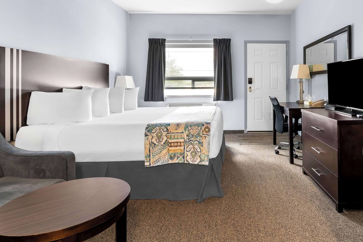 A hotel room with a bed, a desk, a chair, a TV, and a window with curtains.