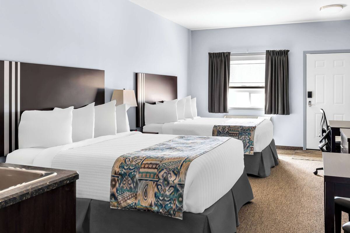 A hotel room with two beds, a desk, and a window with curtains.