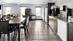 A modern kitchen with a dining area, featuring a long table, chairs, and a refrigerator. - SureStay Studio by Best Western Hardisty (Hardisty)