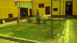 Un patio con un pequeño césped, algunas macetas y un par de sillas de mimbre.