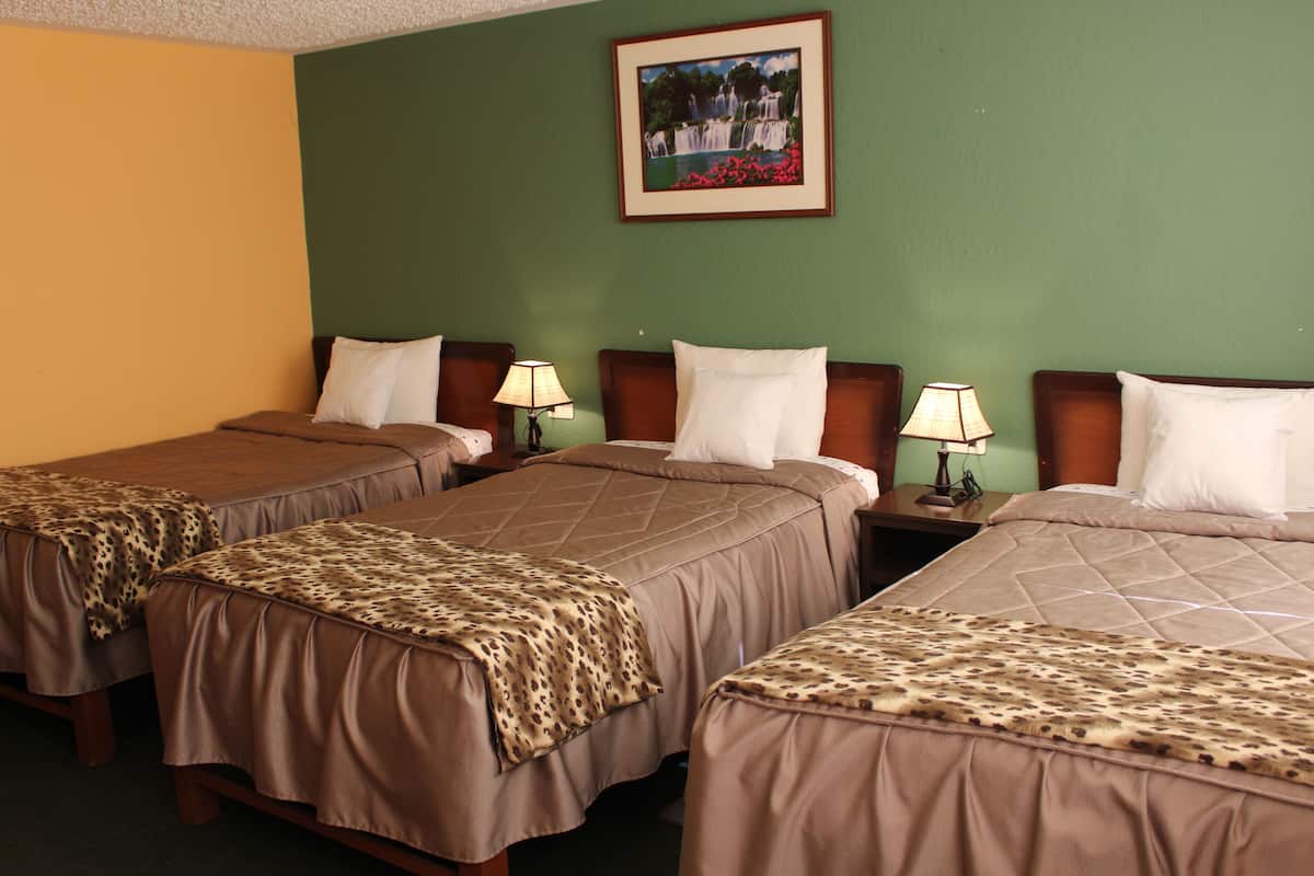 Una habitación de hotel con tres camas individuales, cada una con una colcha marrón y una manta de estampado de leopardo. Hay mesitas de noche con lámparas y un cuadro en la pared.