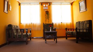 Una habitación con dos sillas de madera, una mesita con un florero y una ventana con cortinas.