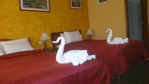 Habitación de hotel con dos camas, cada una con una colcha roja y almohadas blancas. Hay dos cuadros en la pared, una lámpara en cada mesita de noche y una decoración de toallas con forma de cisne en las camas.