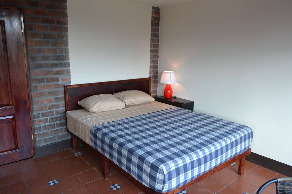 A bedroom with a wooden bed, a red lamp, and a brick wall.