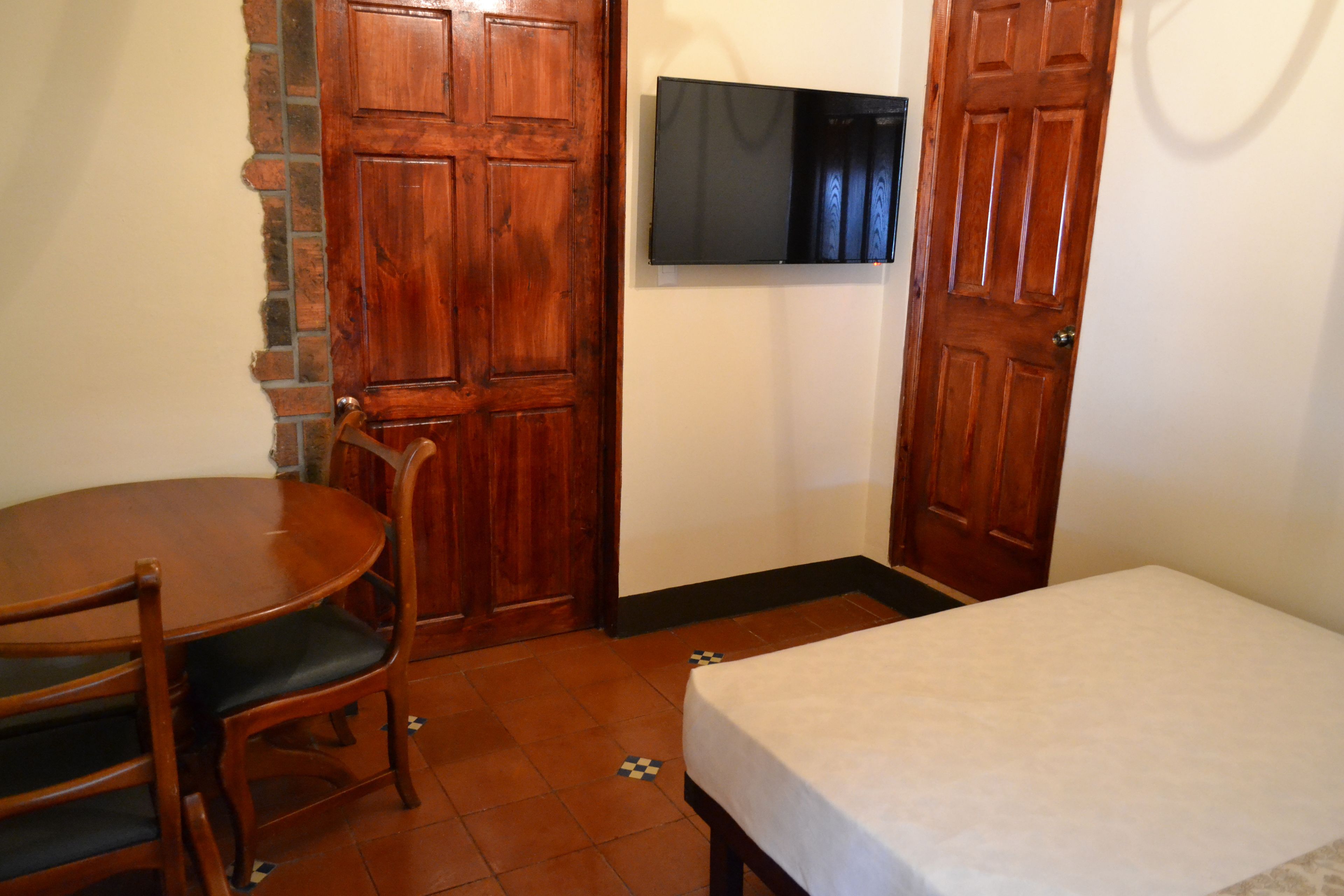 Une pièce avec une table et des chaises en bois, un lit et un téléviseur fixé au mur.