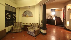 A lobby with two armchairs, a fan, and a staircase leading to the Columbus area. - Hotel Columbus (San José)