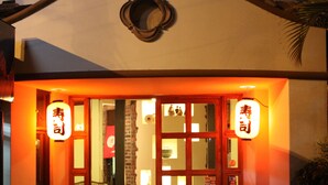 A traditional Japanese entrance with wooden doors and lanterns, leading to an interior with a sofa and brick wall. - Hotel Columbus (San José)