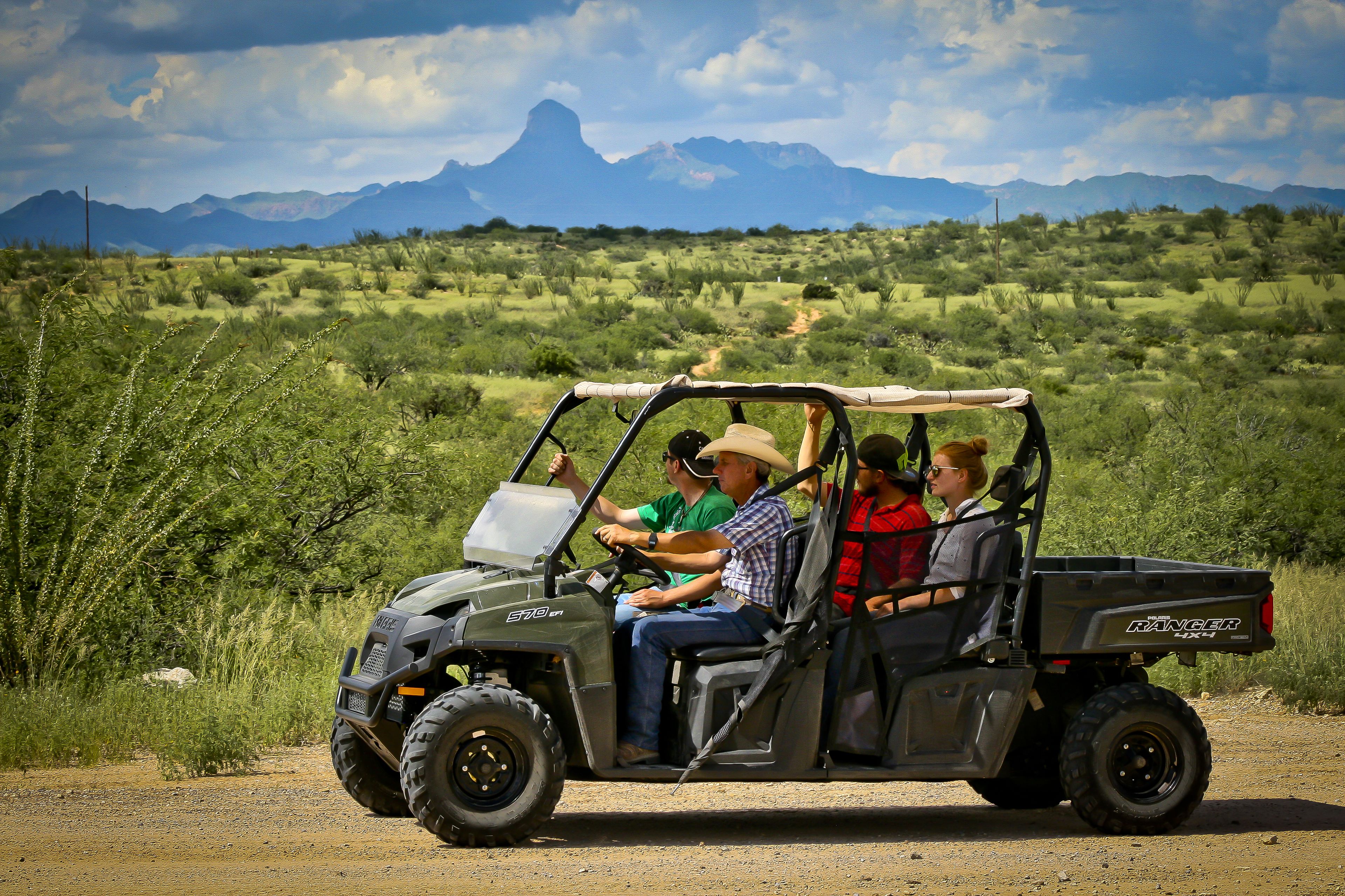 A utility vehicle with a roof and side windows, labeled "RANGER HX4," parked on a dirt road with a mountainous landscape in the background.