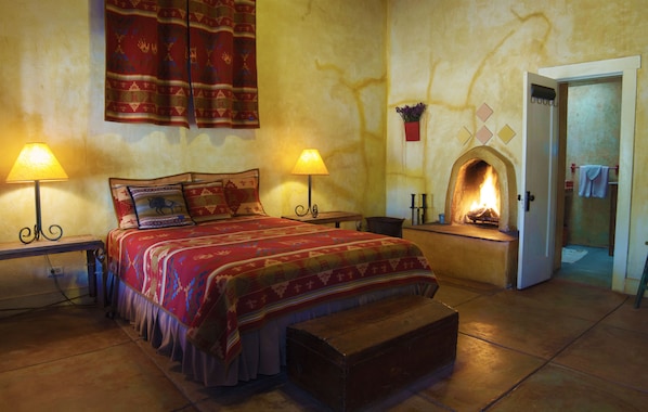 A cozy bedroom with a bed, two bedside lamps, a fireplace, and a bench.