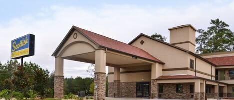 Um hotel com entrada coberta, pilares de pedra e uma placa indicando 'Scottish Inns & Suites'.