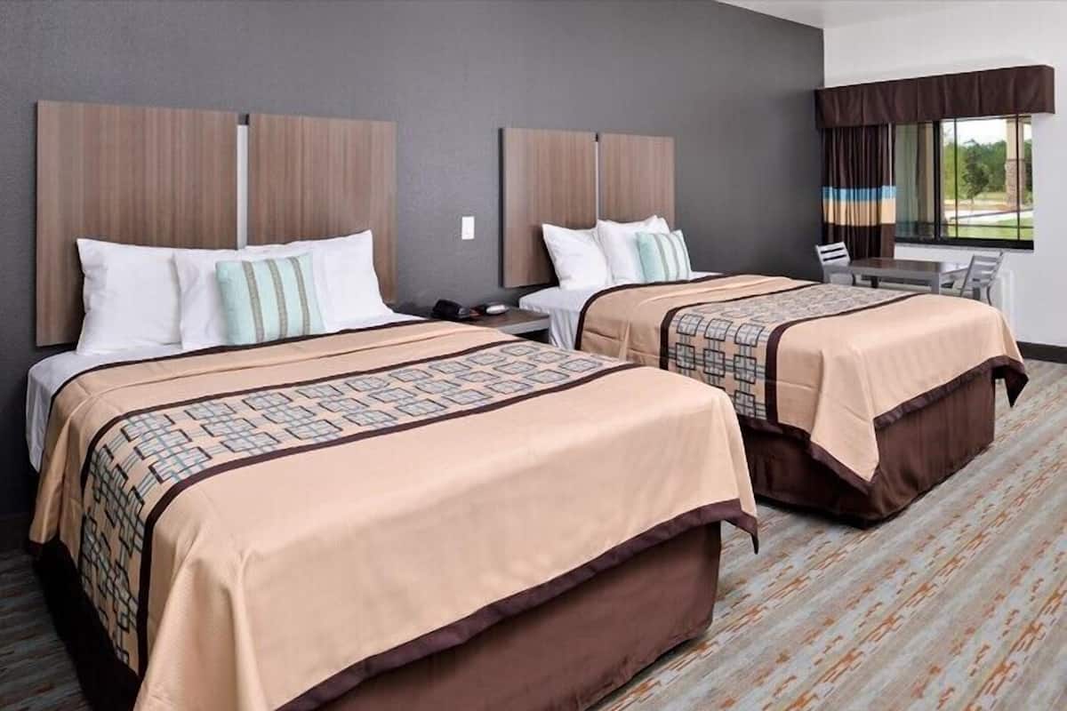 A hotel room with two beds, a small table, and a window with curtains.