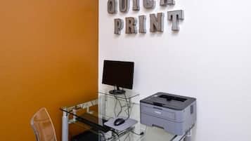 A computer desk with a monitor, keyboard, mouse, and printer against a wall with "QUICK PRINT" signage.