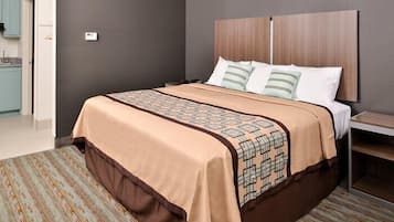 Habitación de hotel con una cama grande, cabecera de madera, colcha estampada y vistas al baño.