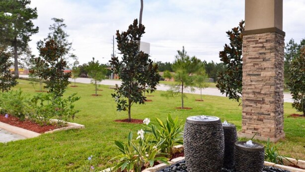 Un jardín ajardinado con un pilar de piedra, una fuente de agua y diversas plantas.
