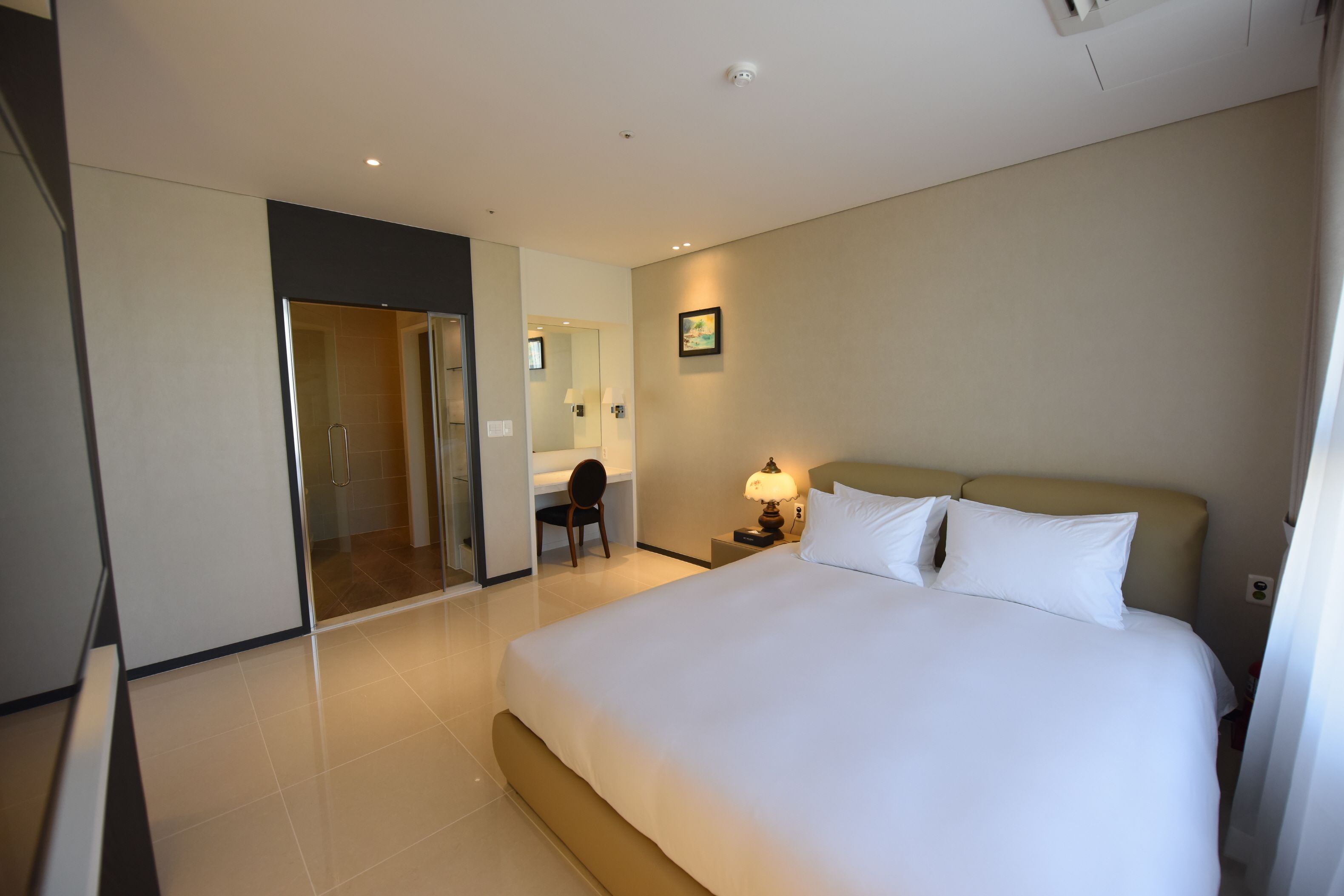 A hotel room with a large bed, a desk, a chair, a lamp, and a door leading to a bathroom.