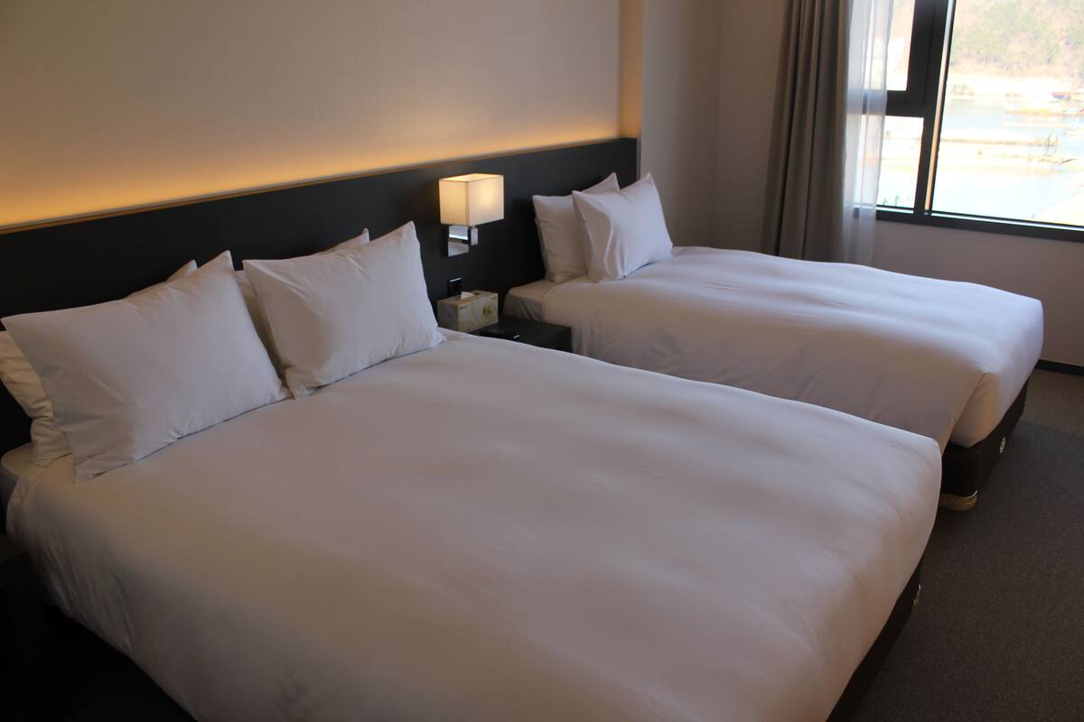 Ein Hotelzimmer mit zwei Betten, einem Nachttisch mit Lampe und einem Fenster mit Vorhängen.