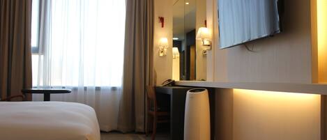 Une chambre d’hôtel avec un lit, un bureau, une chaise, une télévision et une lampe.
