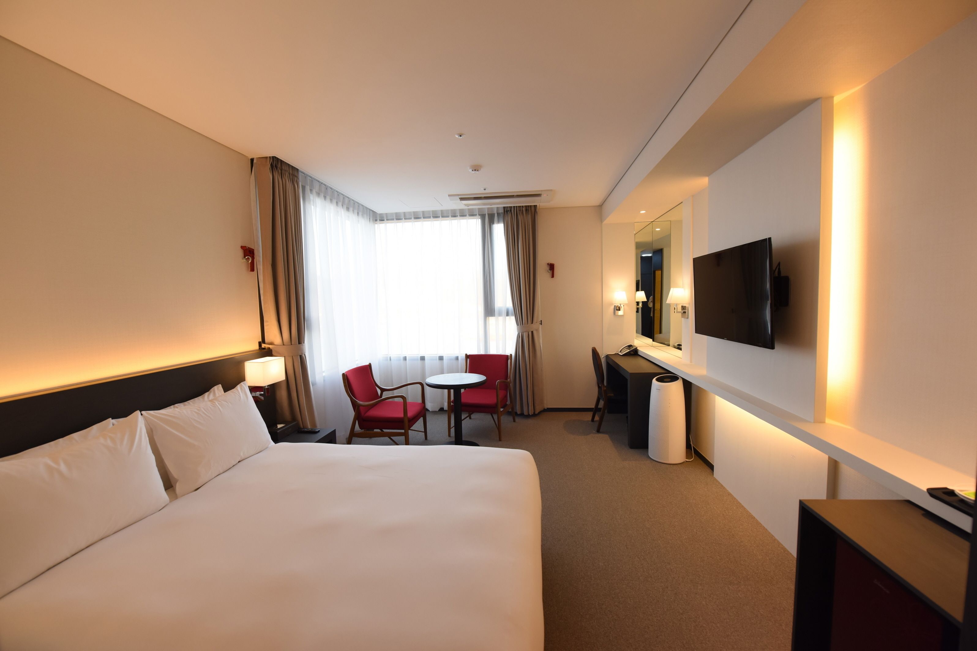 A hotel room with a large bed, a desk, a chair, a TV, and a window with curtains.