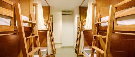 Un pasillo con literas y escaleras de madera que conduce a una habitación con aire acondicionado.