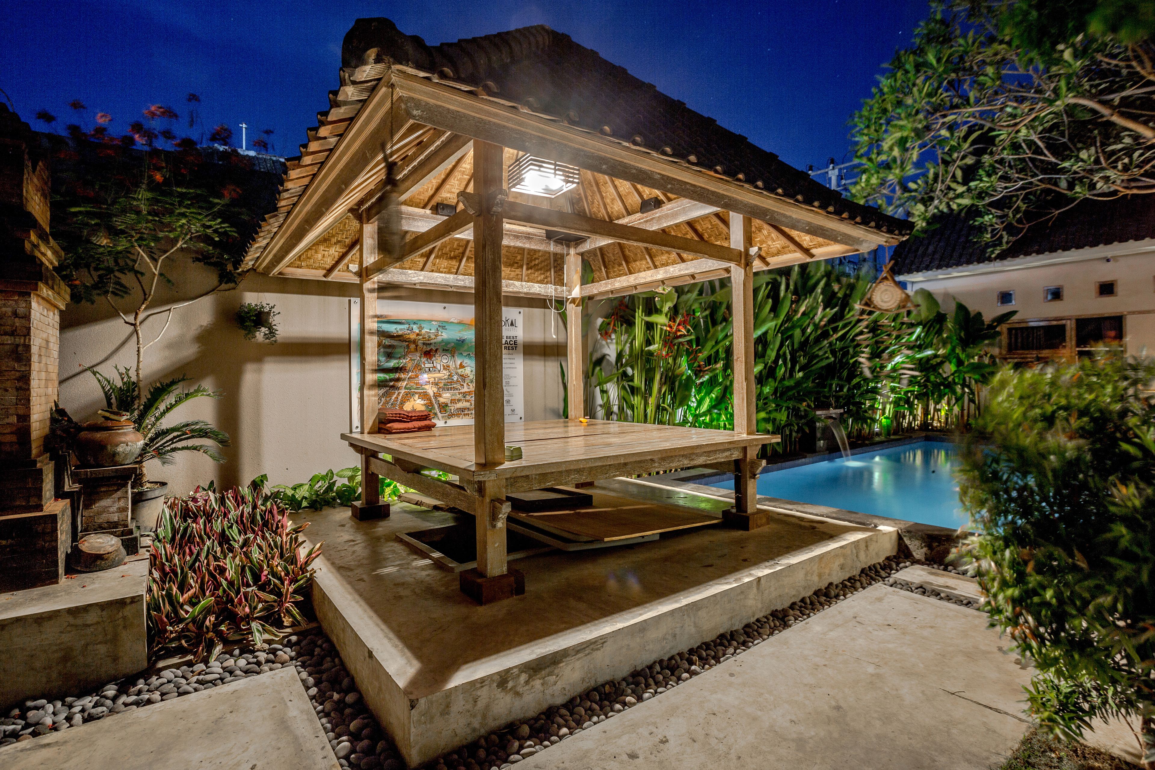 Un quiosco de madera con cerramiento de vidrio, piscina y plantas tropicales.