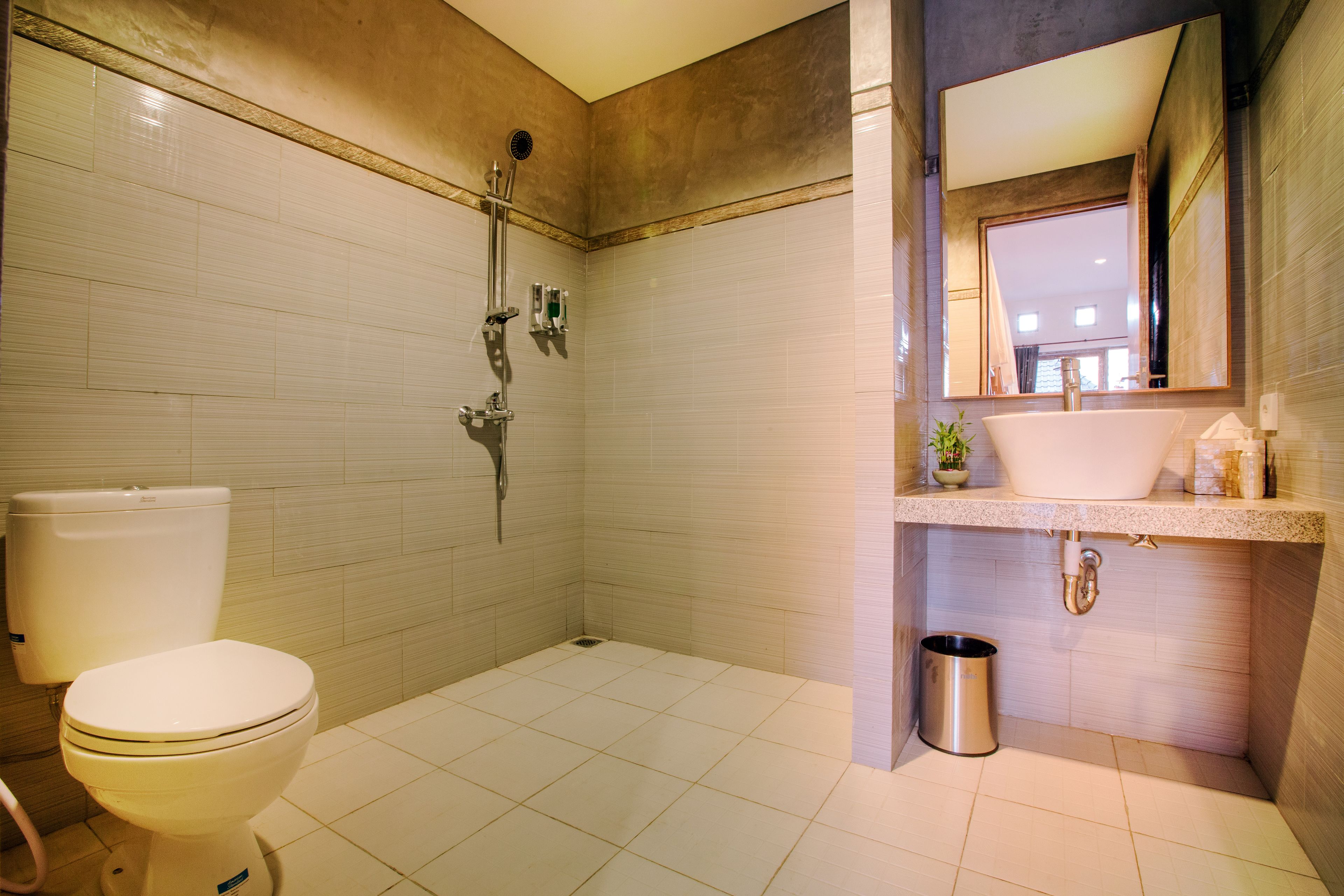 Et badeværelse med toilet, bruser, håndvask og spejl.