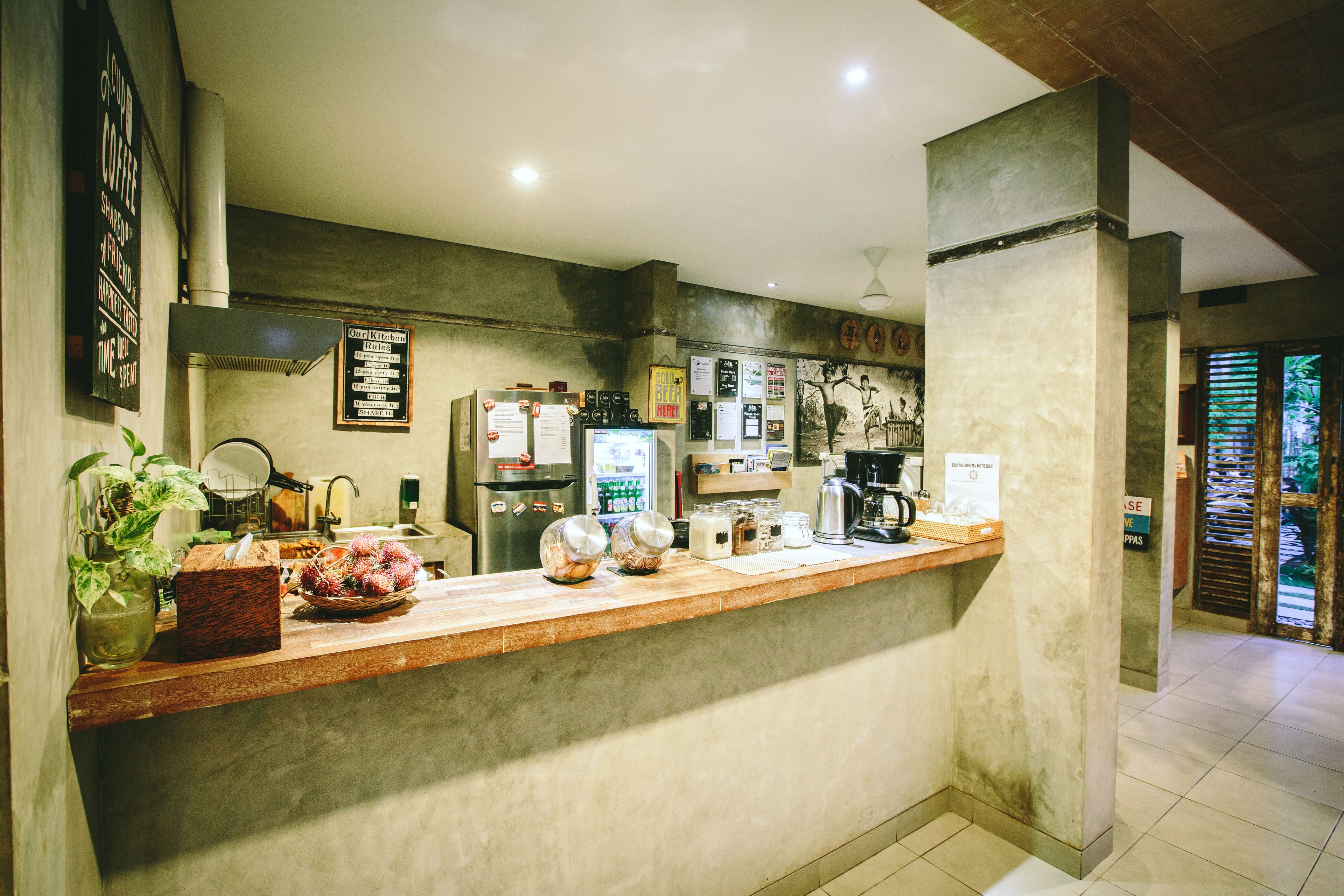 A coffee shop counter with a menu board, a refrigerator, a coffee machine, and a plant.