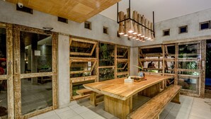 Um quarto amplo com uma grande mesa de madeira, bancos e várias janelas com molduras de madeira.